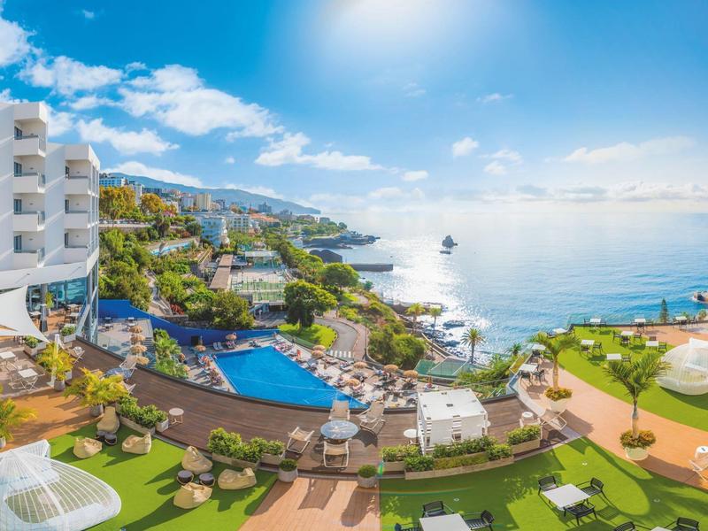 Luxe hotel met zwembaden en zeezicht onder een zonnige hemel.