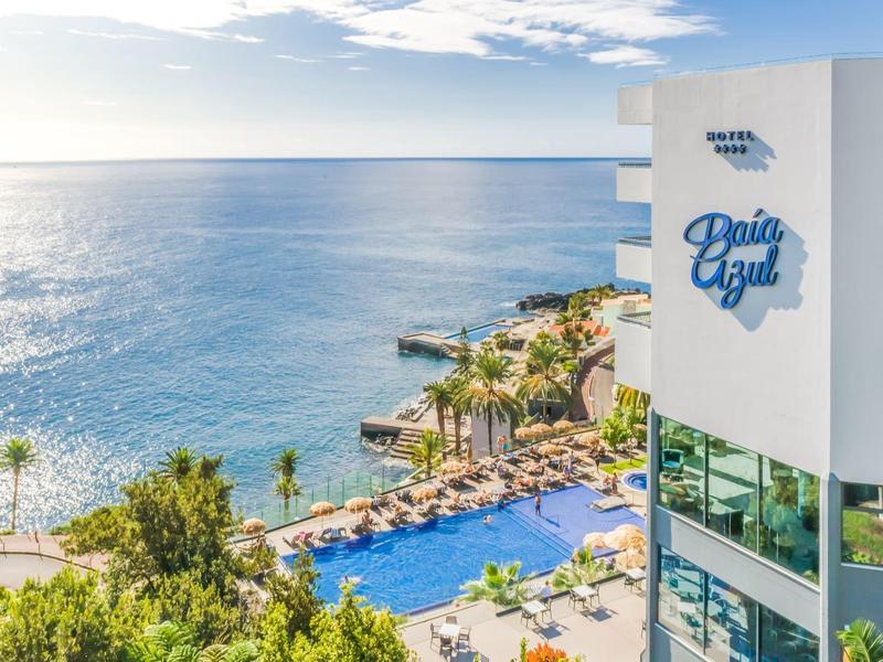 Hotelgebouw met zwembad en uitzicht op rustige blauwe zee bij zonsondergang.