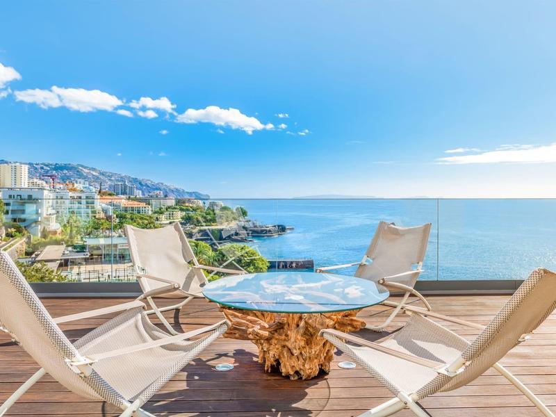 Terras met moderne stoelen met uitzicht op de zee onder een heldere hemel.