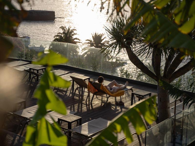 Zonsondergang boven een terras met tafels en stoelen omgeven door planten aan het water.