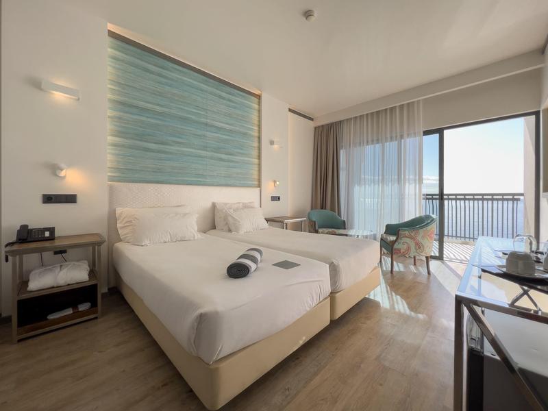 Moderne hotelkamer met twee bedden, ramen van vloer tot plafond en balkon met zeezicht.