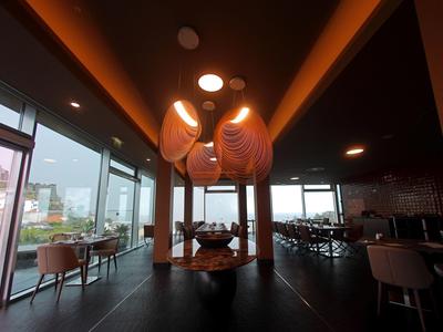 Modernes Restaurant mit großen Fenstern, dunkelgraßen Wänden, orange Beleuchtung und stilvollen Lampen.