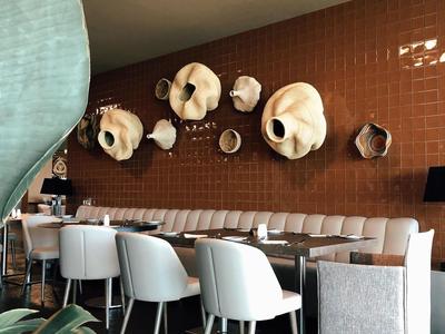 Moderne Gaststätte mit weißen Stühlen, brauner Kachelwand und dekorativen Wandvasen in verschiedenen Größen.