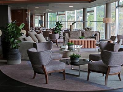 Moderne Lounge mit grauen Sesseln, runden Tischen, hellen Sofas und großen Fenstern.