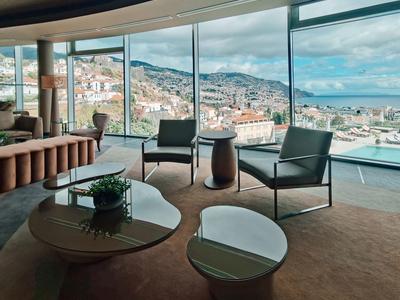 Moderner Wohnraum mit braunem Teppich, Glasfenstern und Blick auf Stadt und Meer bei Tageslicht.