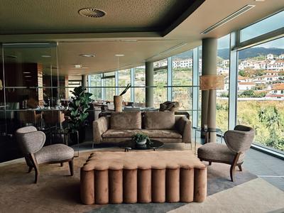 Moderner Wohnraum mit großen Fenstern, braunen Sesseln, Sofa und gepolsterter Bank.