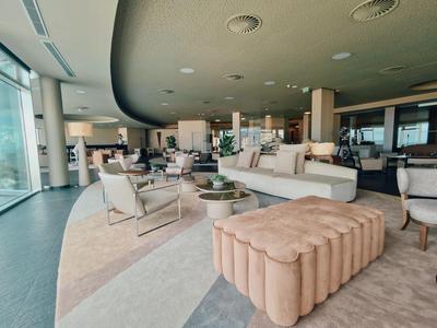 Großer, moderner Aufenthaltsraum mit beigen Sitzmöbeln, Teppich und großen Fenstern für viel Tageslicht.