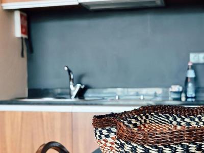 Küchenzeile mit Holzmöbeln, schwarzer Arbeitsplatte, Spüle und geflochtenem Korb auf Tisch.