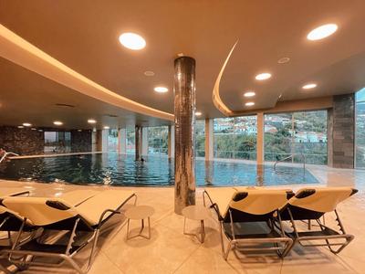 Moderner Innenpool mit großem Fenster, runden Deckenleuchten und Liegestühlen aus Holz und Stoff.