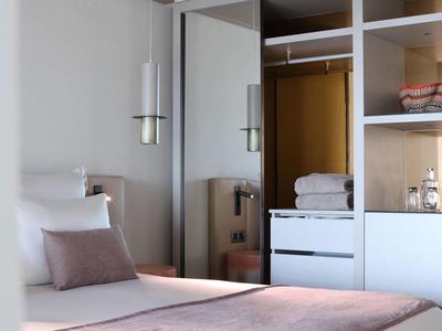 Helles Schlafzimmer mit weißem Bett, rosa Decke, Kissen und offenem Schrank mit Handtüchern.