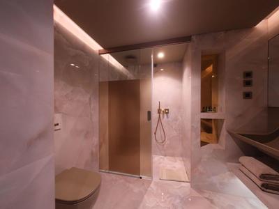 Modernes Badezimmer mit Marmorwänden, begehbarer Dusche, braunen Holzregalen und indirekter Beleuchtung.