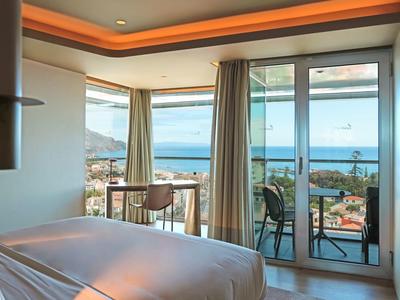 Helles Schlafzimmer mit Balkon, Meerblick und Vorhängen, modernem Deckenlicht und minimalistischem Design.