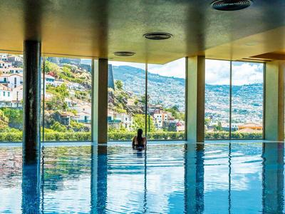 Ein großer Innenpool mit einer Person und Blick auf eine Stadt und Berge durch Glasfenster.