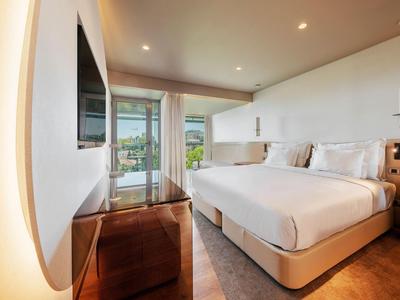 Modernes Hotelzimmer mit großem Doppelbett, Flachbildfernseher und Balkon mit Seeblick.