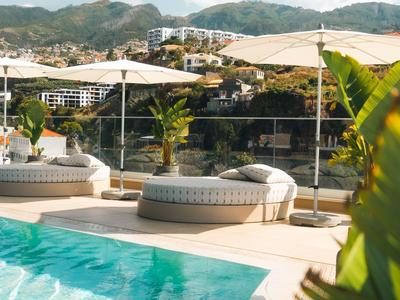 Ein Pool mit rundem Sitzbereich und Sonnenschirmen, umgeben von Bergen und Blauem Himmel.