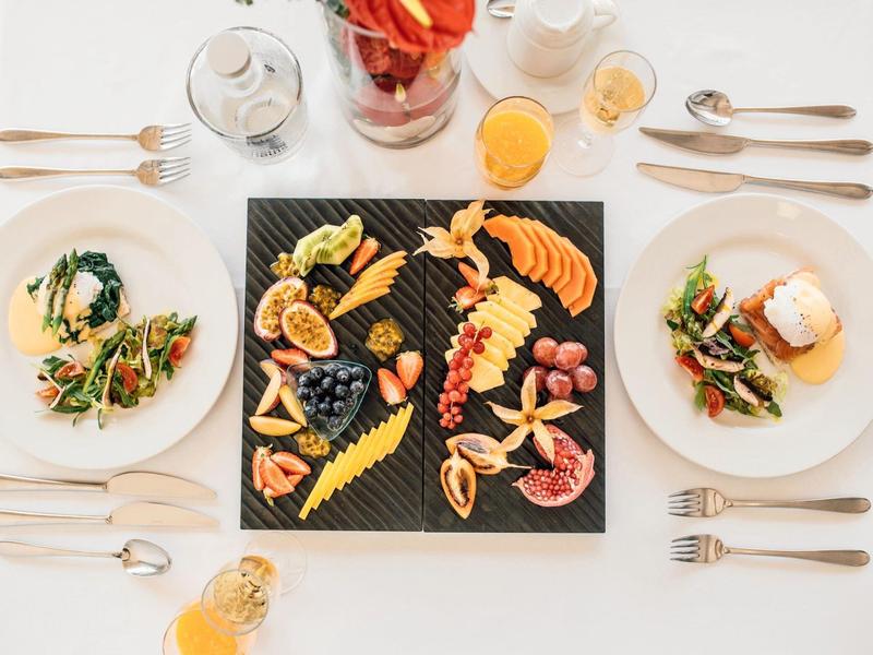 Elegantes Tischgedeck mit bunter Vorspeisenplatte, Salaten und Orangensaft auf weißem Tuch.