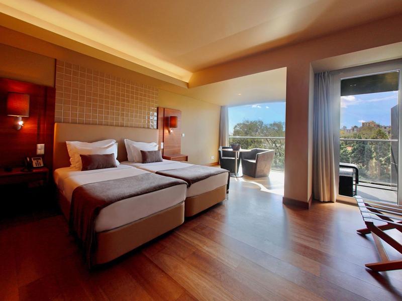 Modernes Hotelzimmer mit zwei Einzelbetten, Holzfußboden und Balkon mit Ausblick auf Bäume.