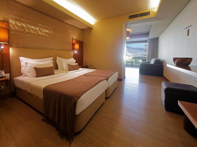 Modernes Hotelzimmer mit Doppelbett, warmen Holztönen und großem Fenster.