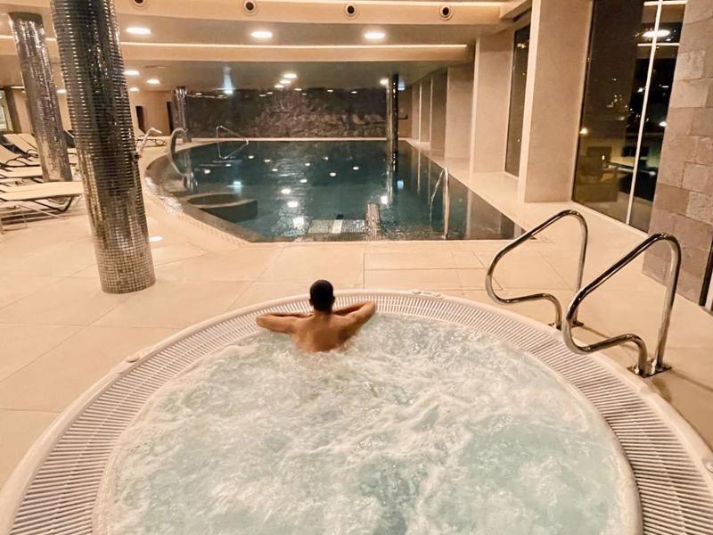 Innenbereich mit großem Pool und rundem, sprudelndem Whirlpool, helle Beleuchtung, ruhige Atmosphäre.