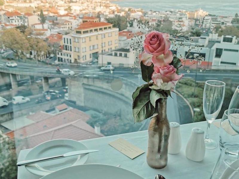 Blick auf Stadt und Meer, gedeckter Tisch mit Dessert und Rosen in Vase im Vordergrund.