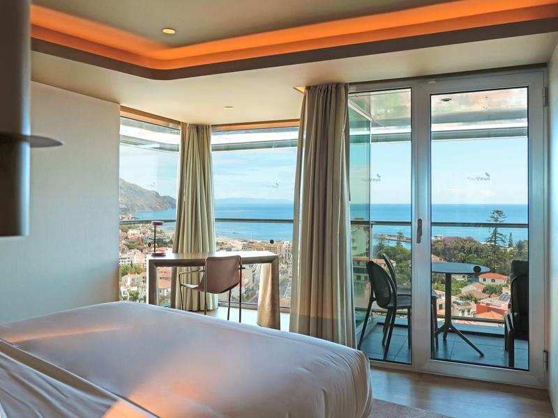 Helles Schlafzimmer mit Balkon, Meerblick und Vorhängen, modernem Deckenlicht und minimalistischem Design.