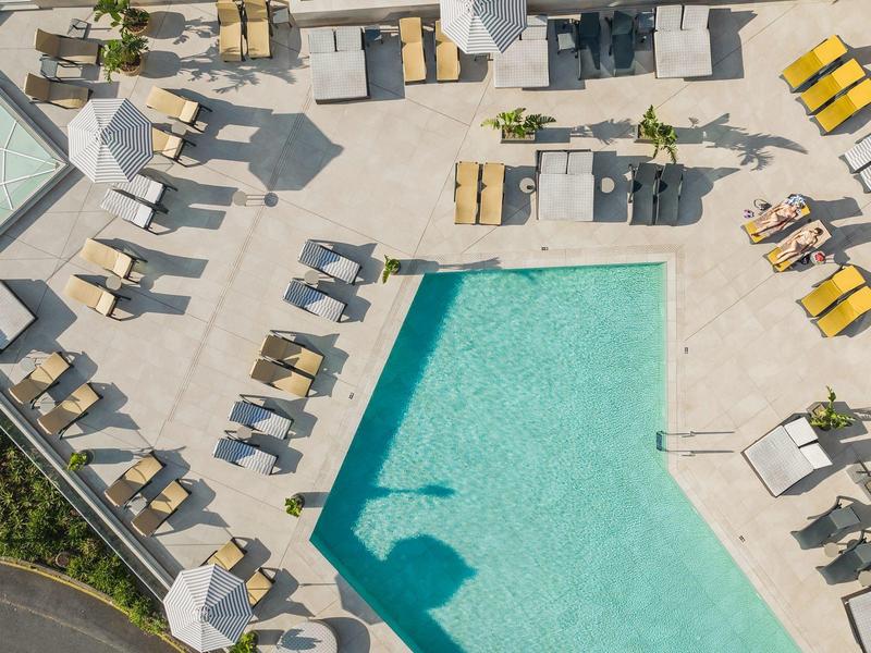 Freizeitbereich mit rechteckigem Pool, Liegestühlen und Sonnenschirmen auf hellem Boden.