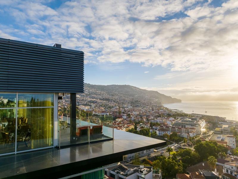 Moderne Terrasse mit Glasgeländer, Stadt und Meer im Tal unter blauem Himmel mit Wolken.