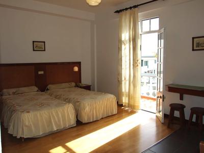 Helles Schlafzimmer mit zwei Einzelbetten, Holzfußboden, Balkon und Vorhängen an der Tür.