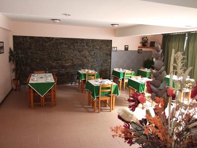 Ein ruhiger Raum mit kleinen Tischen, grünen Tischdecken und einer Steinwand im Hintergrund.