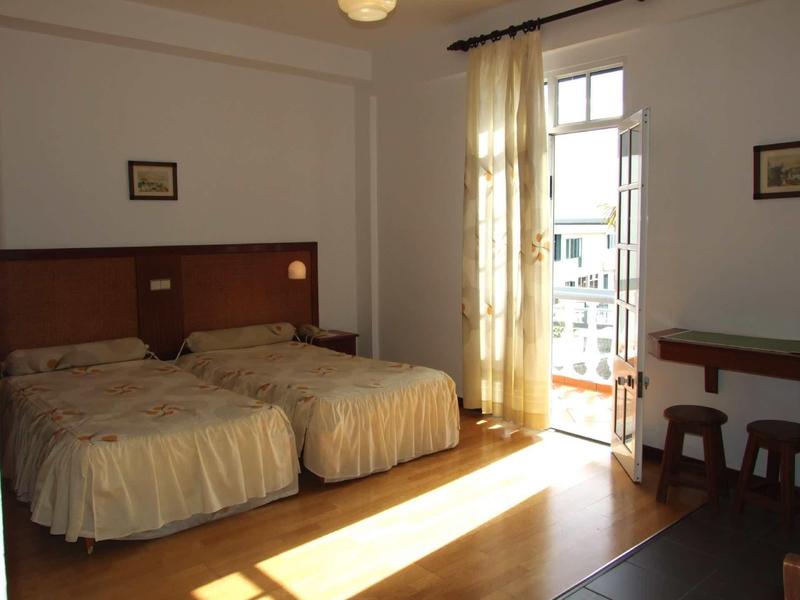 Helles Schlafzimmer mit zwei Einzelbetten, Holzfußboden, Balkon und Vorhängen an der Tür.