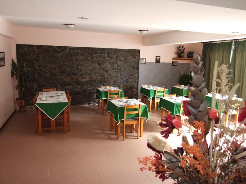 Ein ruhiger Raum mit kleinen Tischen, grünen Tischdecken und einer Steinwand im Hintergrund.