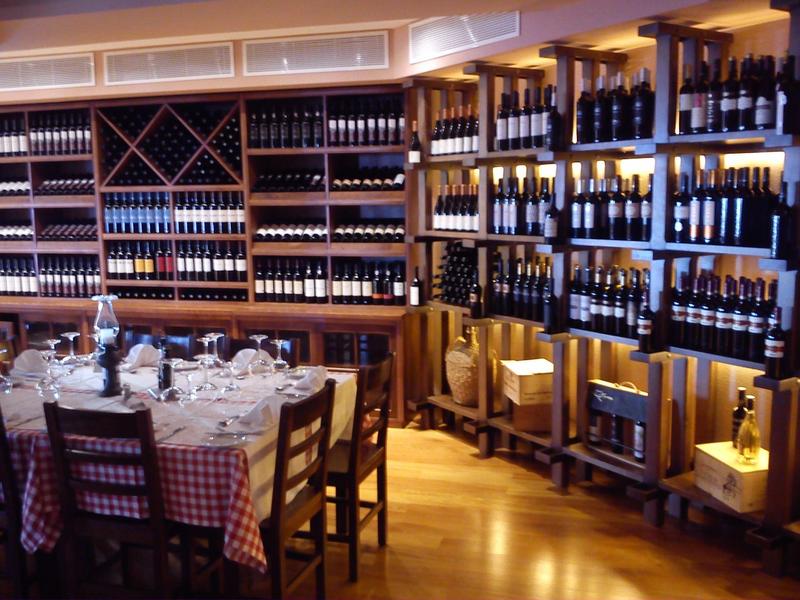 Cantina con mobili in legno, bottiglie di vino sugli scaffali e tavoli apparecchiati con tovaglie a quadri rosse e bianche.