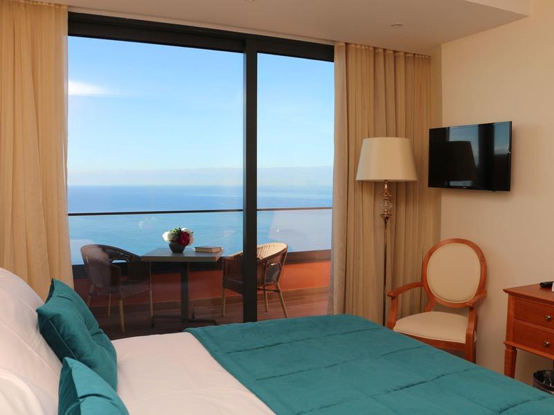 Camera d'hotel moderna con letto, sedia, scrivania e balcone con vista sul mare.