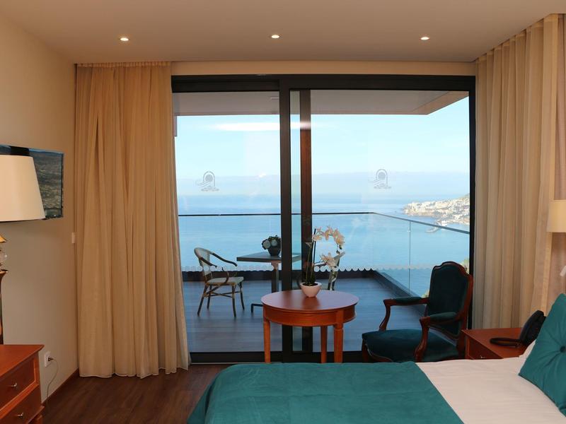 Camera d'hotel con vista mare, balcone e area salotto, arredamento moderno in tonalità calde.