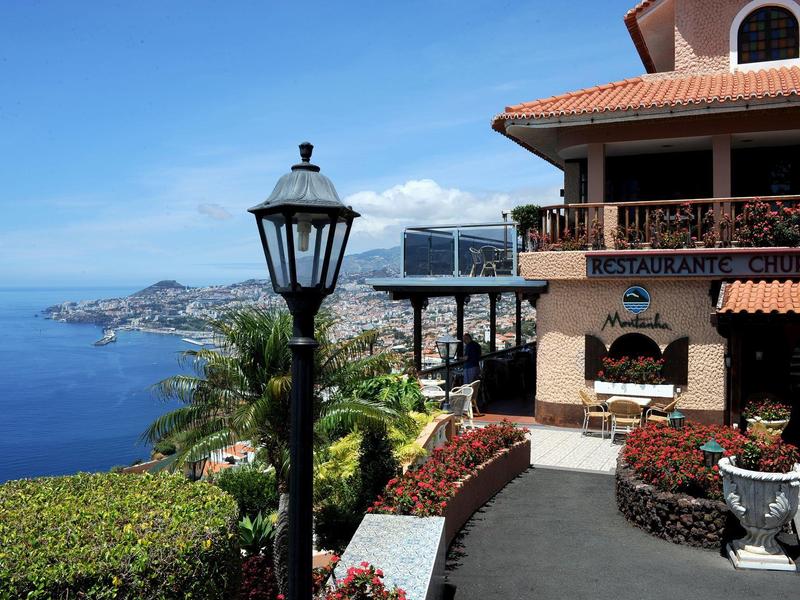Vista sul mare e sulla città da una terrazza con un lampione e una vegetazione rigogliosa.