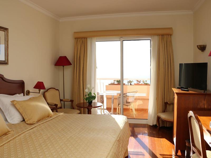 Camera d'albergo luminosa con letto matrimoniale, TV e balcone con vista esterna.