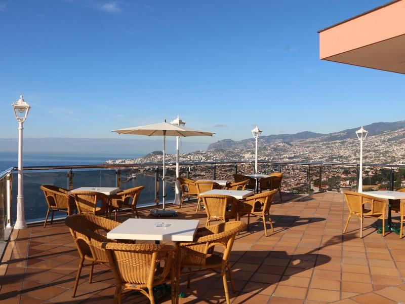 Terrazza sul tetto con tavoli, sedie e ombrelloni con vista sul mare e sulla città.