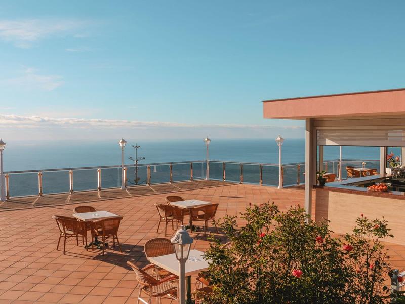 Terrazza con tavoli e sedie con vista sul mare sotto un cielo sereno.