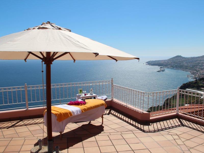 Una terrazza soleggiata con sdraio e ombrellone con vista sul mare e le montagne.