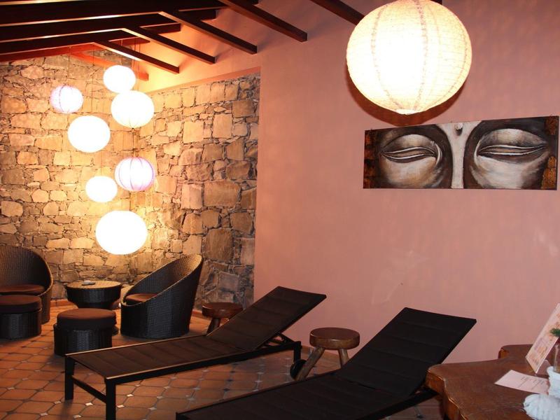 Accogliente terrazza con lettini, sedie e illuminazione calda su una parete in pietra.