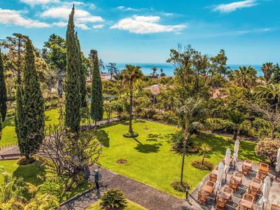 Giardino verde con cipressi snelli, palme e zona salotto in località costiera soleggiata.