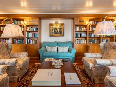 Accogliente sala lettura con scaffali, tappeto, divano e poltrone in luce calda.