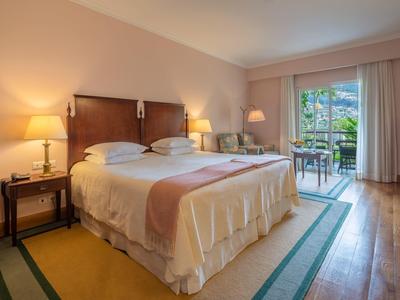 Camera d'hotel accogliente con grande letto matrimoniale, comodini e balcone con vista sul verde.