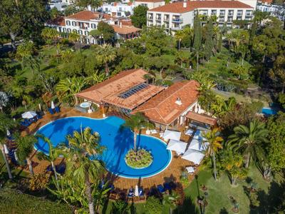 Vista aerea di un hotel con piscina circondato da palme e paesaggio verde.