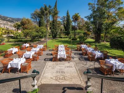 Sedute all'aperto con tavoli e tovaglie bianche in un giardino sotto un cielo sereno.