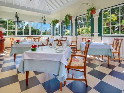Sala da pranzo luminosa con pavimento a scacchiera, tavoli con tovaglie bianche e sedie di legno.