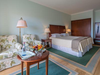 Camera d'albergo accogliente con letto matrimoniale, due poltrone, tavolo e illuminazione calda.