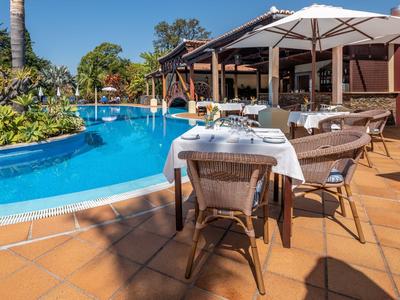 Essbereich mit gedecktem Tisch neben blueem Pool und Sonnenschirmen in tropischer Hotelanlage.