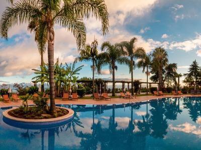 Grande piscina con palme e aree salotto sotto un cielo colorato al tramonto.