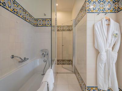 Bagno bianco con vasca, piastrelle decorative e un accappatoio bianco appeso al muro.